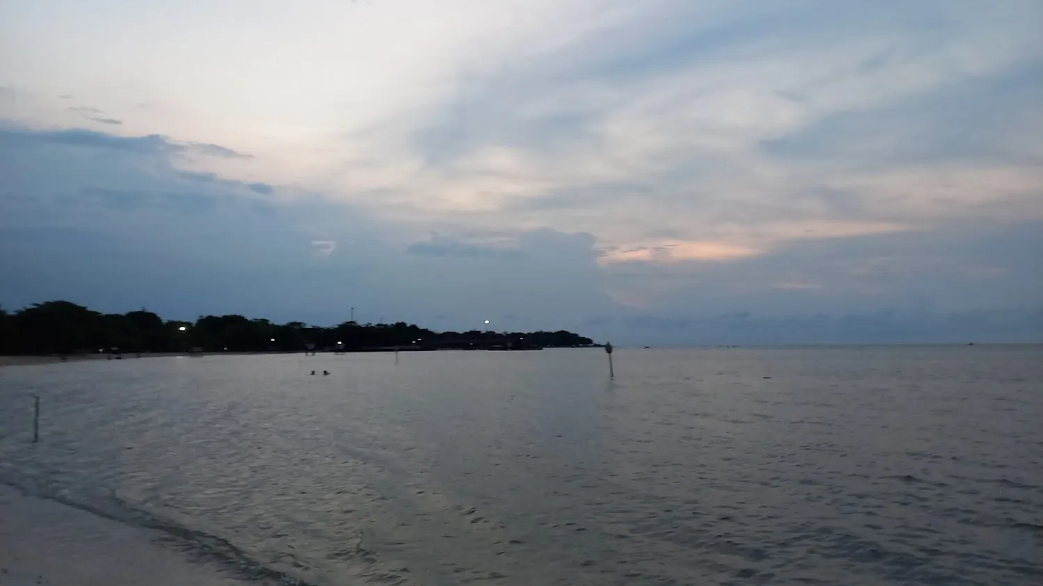 Air laut tenang dan garis pantai berpasir di Pantai Bandengan Jepara saat senja