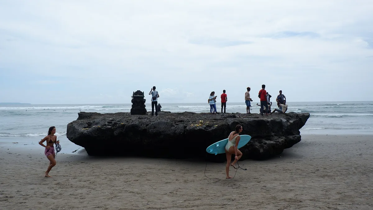 Peselancar dan pengunjung berkumpul di sekitar batu karang besar di Pantai Batu Bolong, Canggu