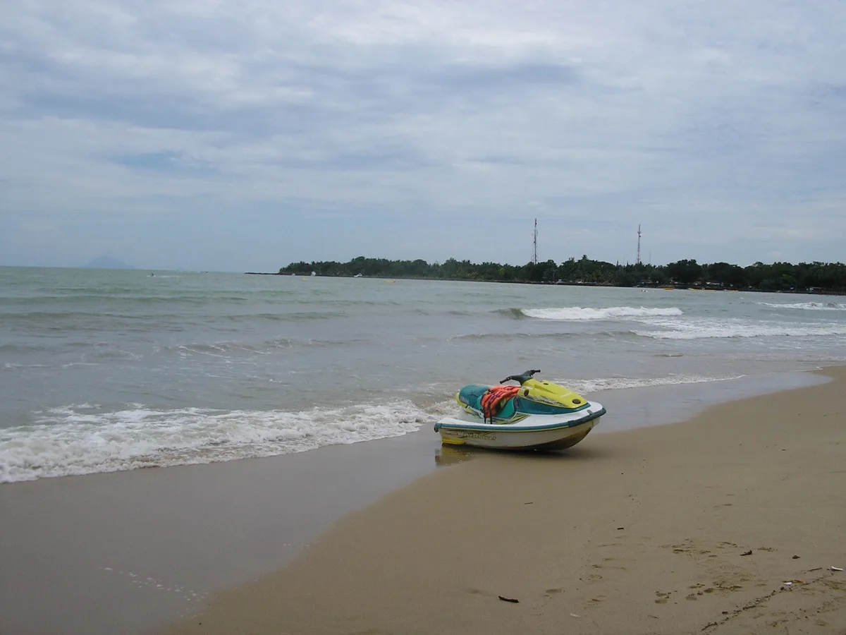 Jetski disandarkan di pasir basah tepi Pantai Carita dengan garis pantai berpohon di kejauhan