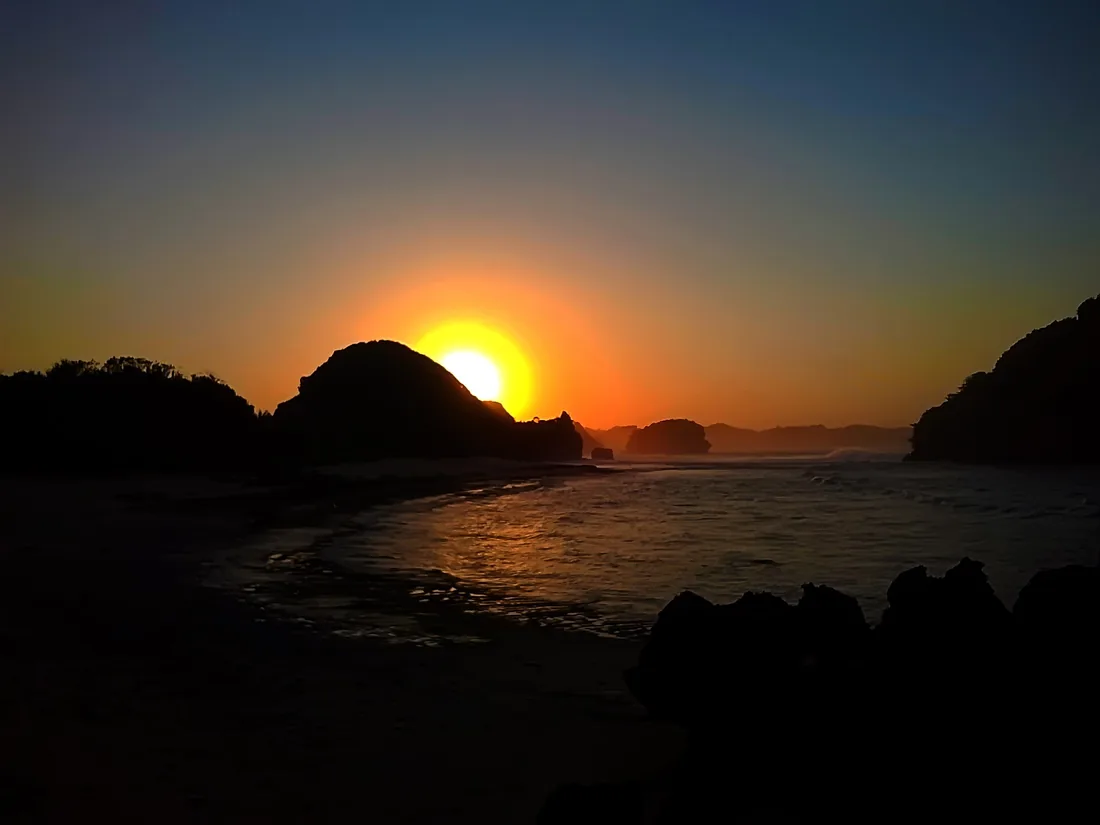Matahari terbit di Pantai Goa Cina, Kabupaten Malang, dengan siluet pulau karang di garis pantai