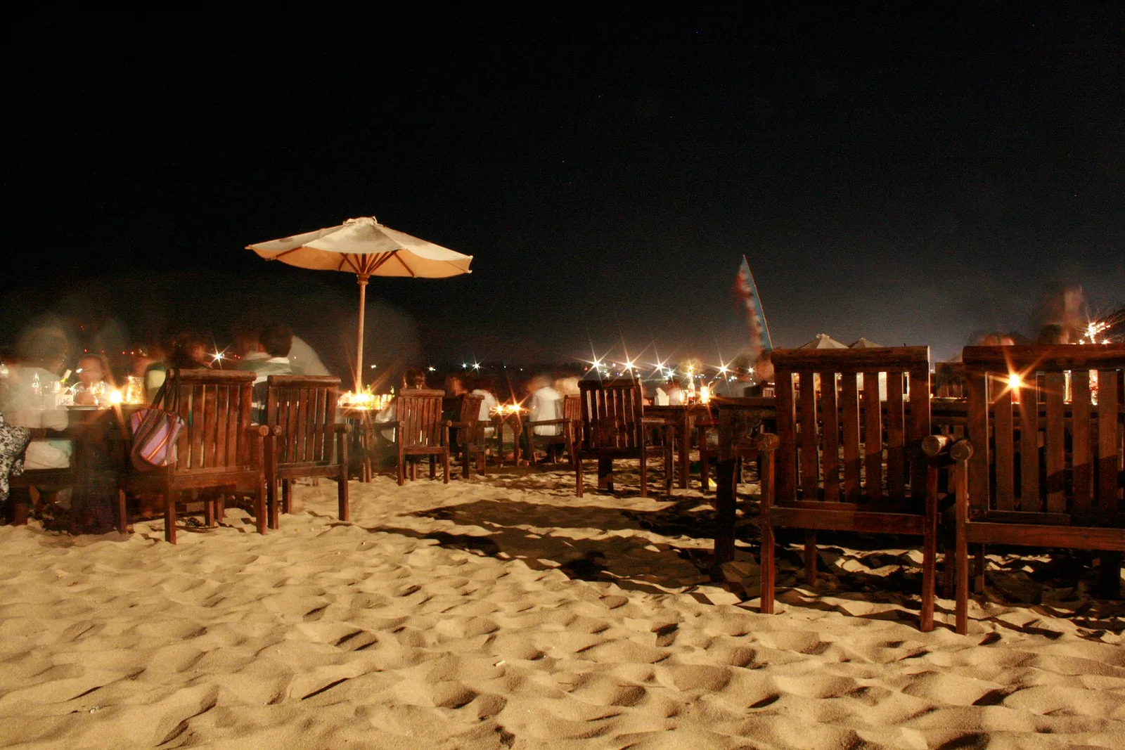Meja dan kursi kayu berlampu lilin ditata langsung di atas pasir Pantai Jimbaran pada malam hari