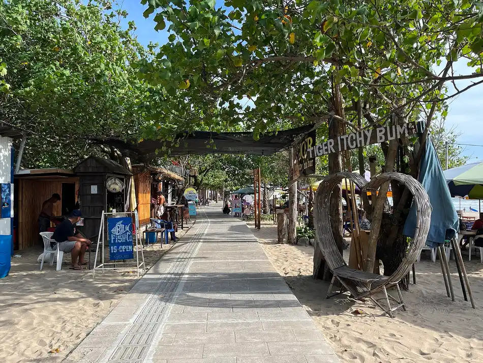 Jalur pejalan kaki di tepi Pantai Legian dengan deretan kios kayu dan pepohonan rindang