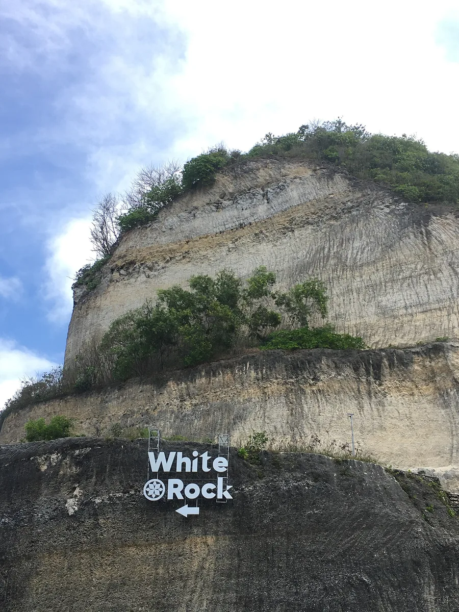 Tebing kapur tinggi berlapis di Pantai Melasti Ungasan dengan papan penunjuk arah bertuliskan White Rock di bagian bawah