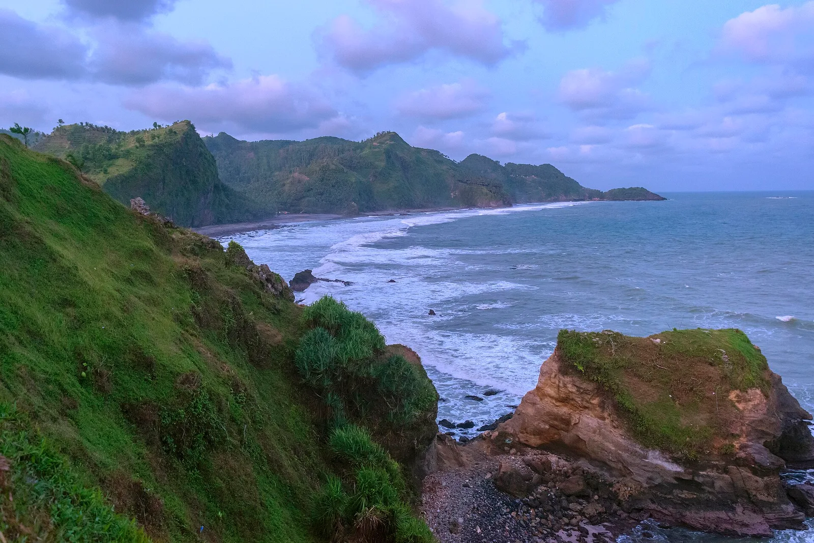 Suasana senja di Pantai Menganti dengan deretan bukit hijau memanjang dan batu karang besar di tepi air