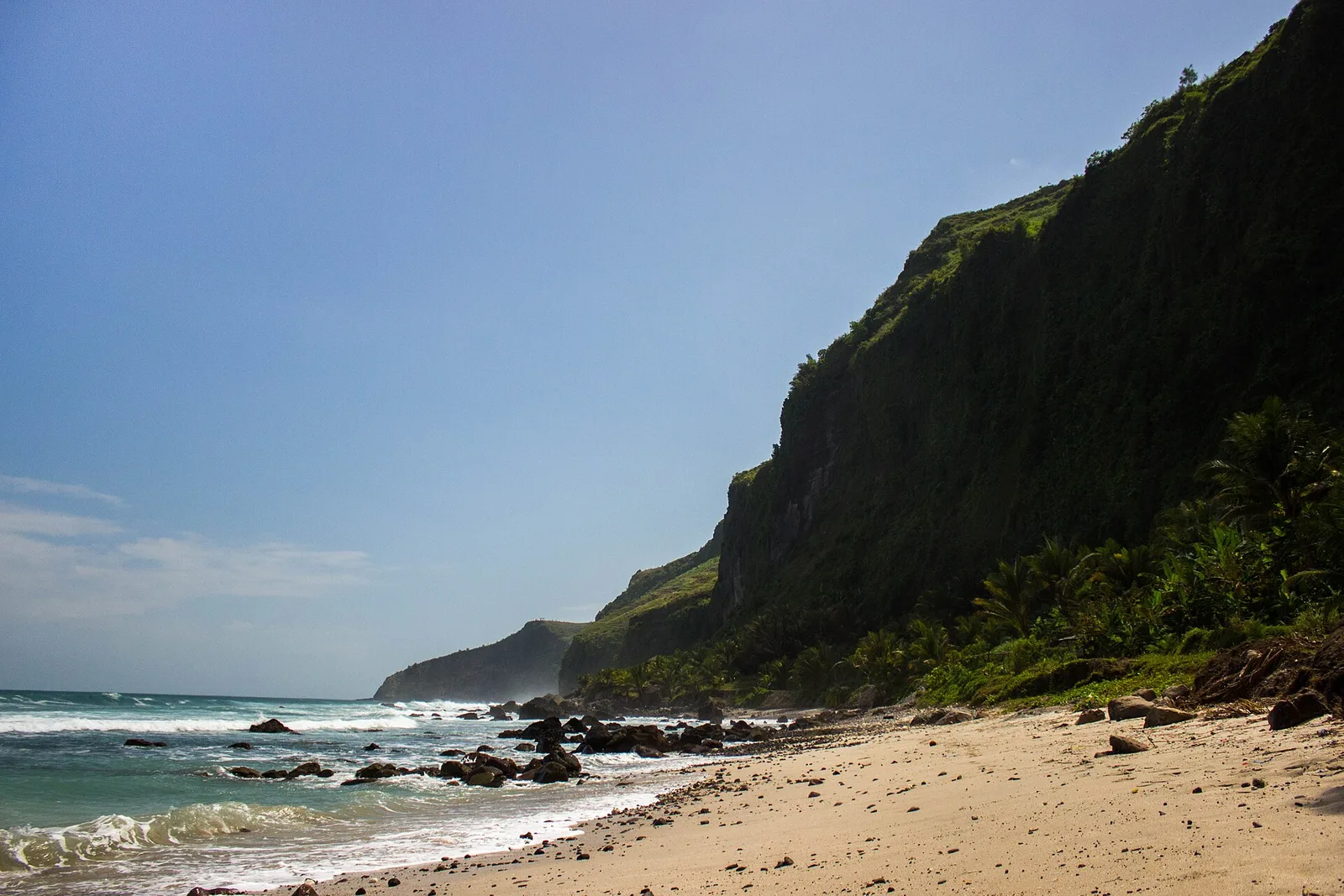 Hamparan pasir Pantai Menganti dengan tebing karang berselimut rumput hijau menjulang di sisi kanan