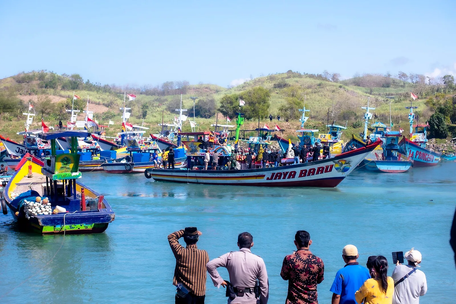 Perahu nelayan berhias bendera merah putih membawa rombongan warga saat upacara larung sesaji di Pantai Tambakrejo Blitar, ditonton warga dari tepi kolam labuh