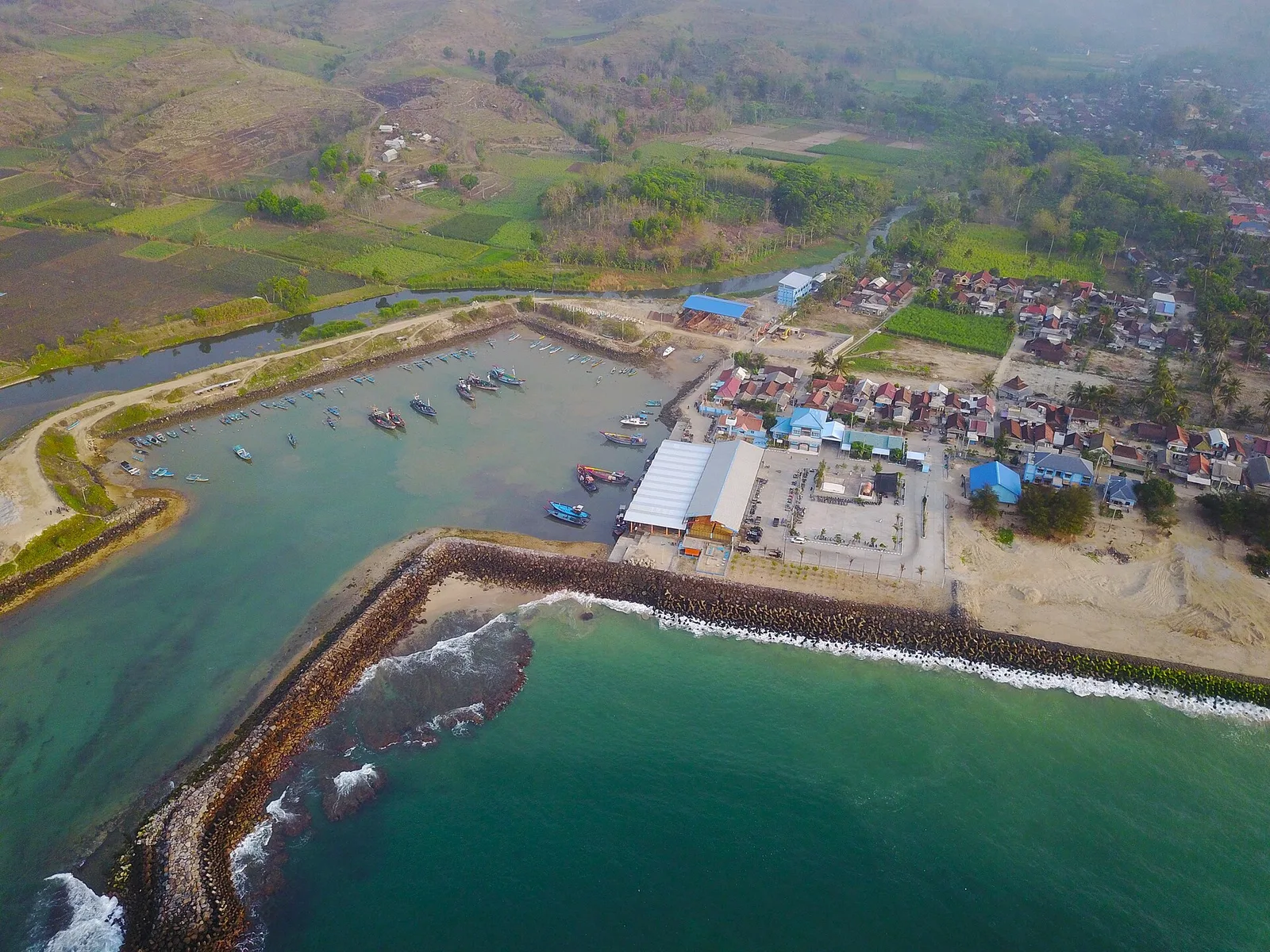 Foto udara Pelabuhan Perikanan Pantai Tambakrejo di Kecamatan Wonotirto, Blitar, memperlihatkan kolam labuh, pemecah gelombang batu, permukiman nelayan, dan ladang di perbukitan