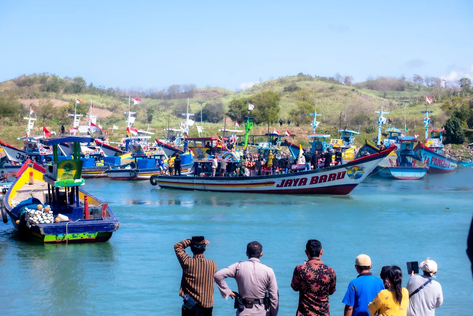 Perahu nelayan berhias bendera dan warga menonton dari tepi saat upacara Larung Sesaji di Pantai Tambakrejo