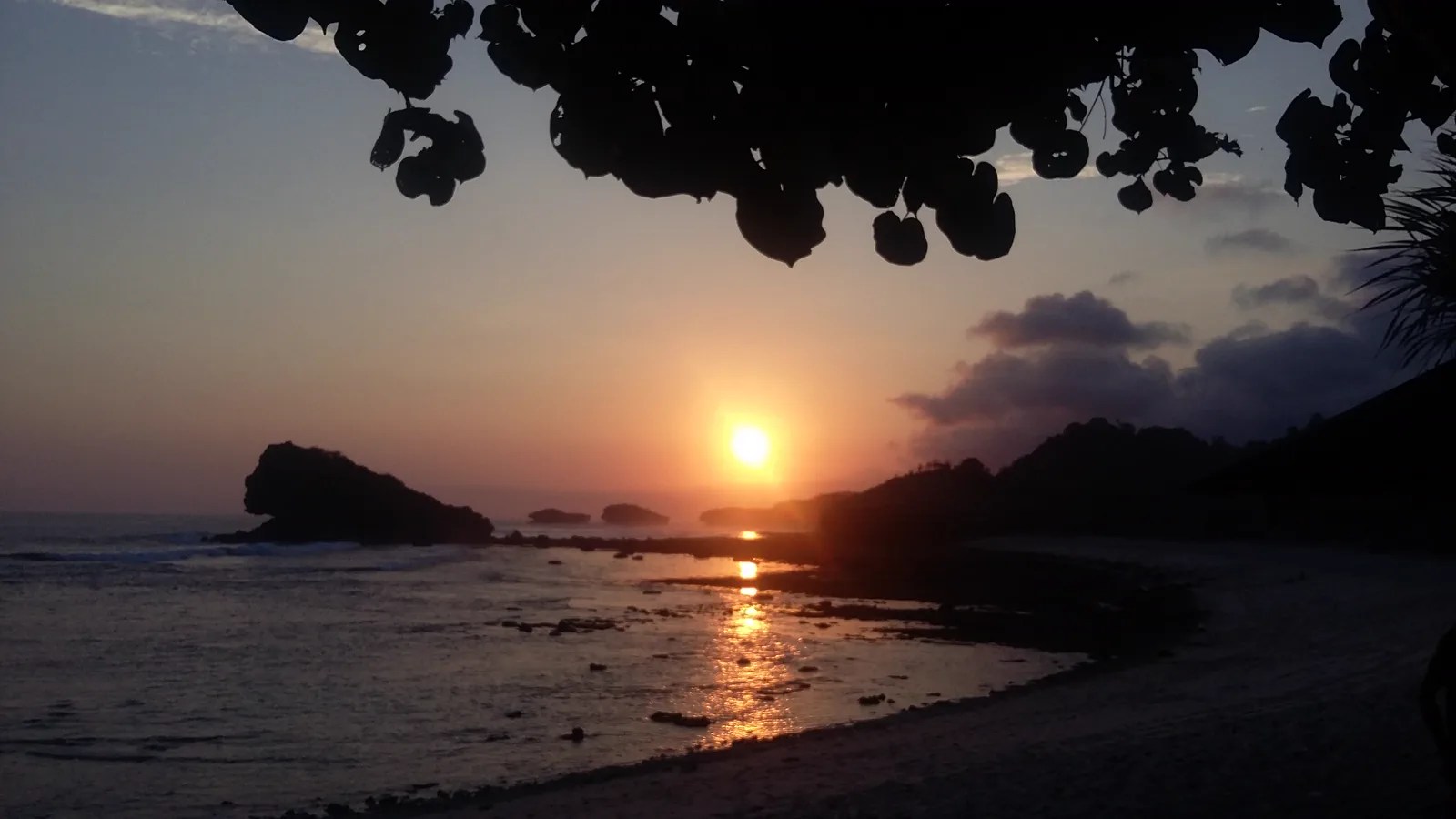 Matahari terbenam di balik pulau karang Pantai Watu Karung, memantul di genangan air di hamparan karang yang tersingkap saat surut