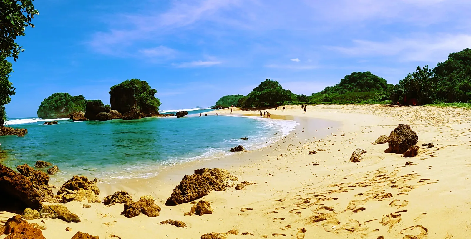 Teluk berpasir putih di Pantai Watu Leter dengan tiga pulau karang bervegetasi di tengah laut dan bukit hijau di sisi kanan