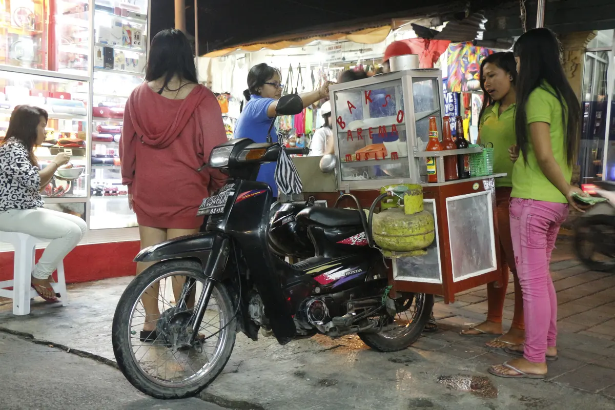 Deretan kios dan gerobak jajanan di gang kawasan Kuta, Bali, dengan pengunjung berbelanja