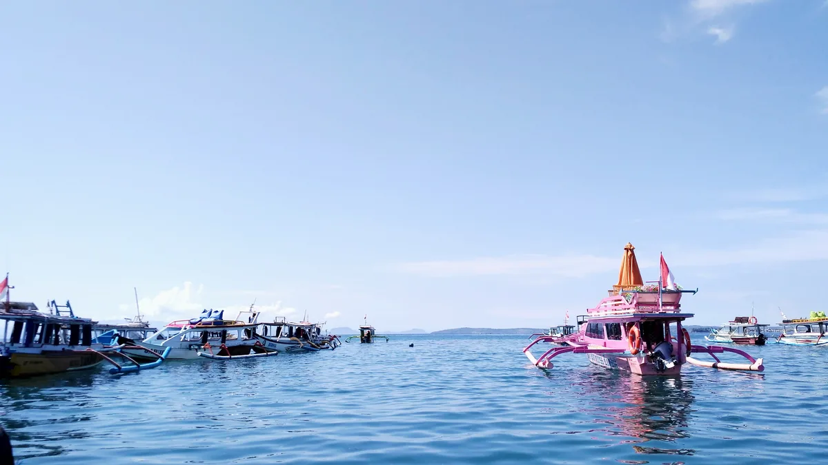 Perahu-perahu kayu bercadik berkumpul di perairan dekat dermaga Tanjung Luar, salah satunya bercat merah muda