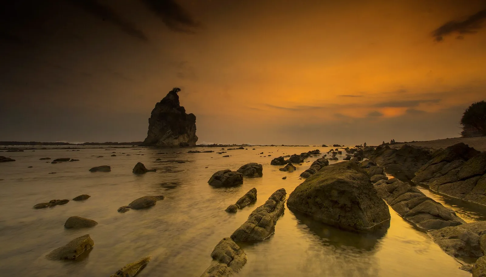 Batu karang besar menjulang di antara hamparan karang datar saat matahari terbenam di pesisir Sawarna