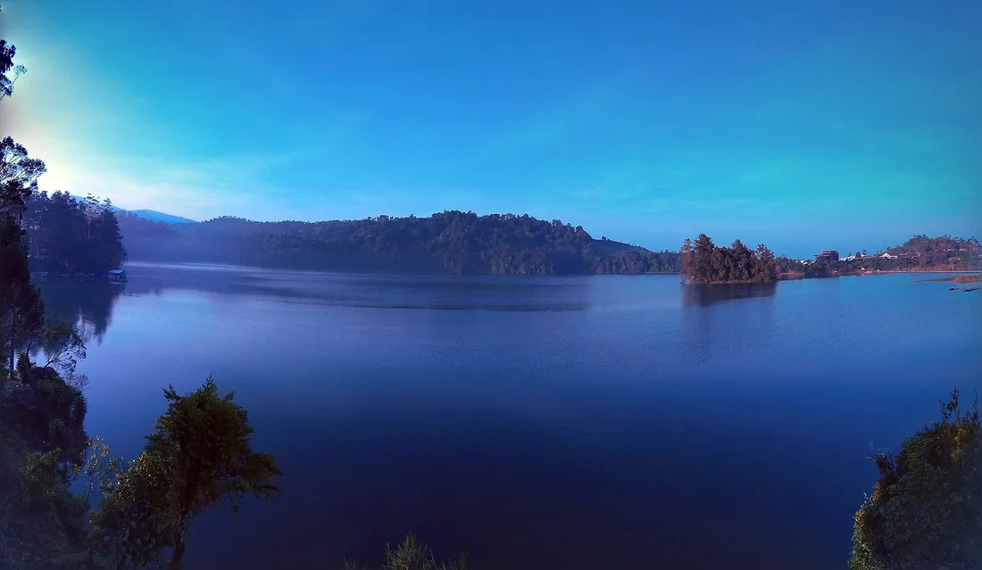 Danau Situ Patenggang di Ciwidey pada pagi hari dengan permukaan air tenang dan bukit berhutan di seberang