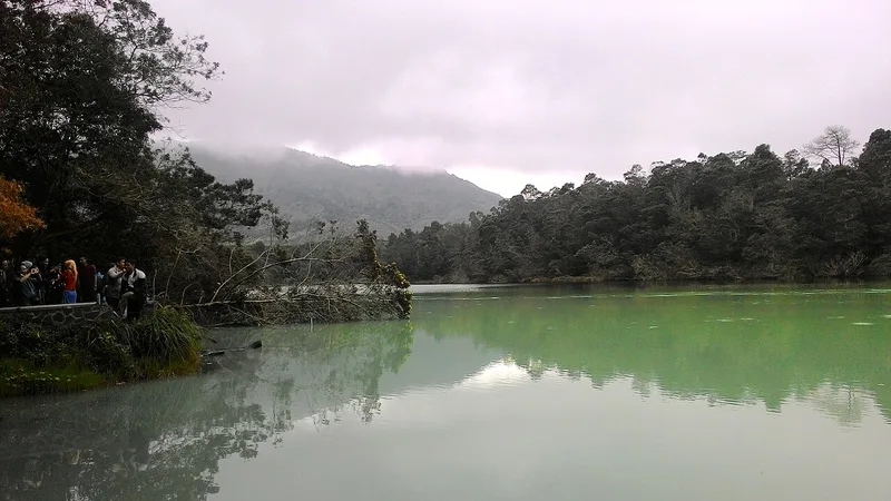 Tepi Telaga Warna dengan air kehijauan, pepohonan rapat, dan pengunjung di jalur pinggir telaga