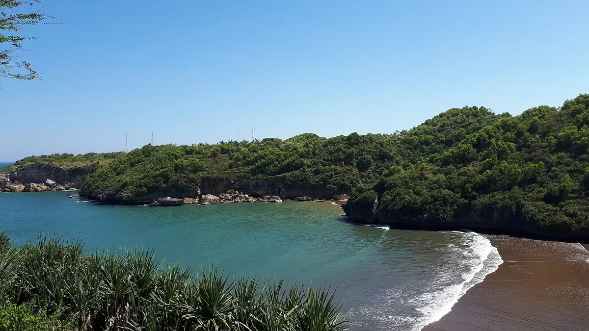 Teluk Pantai Baron berbentuk huruf U diapit bukit karang berhutan dengan air laut hijau kebiruan