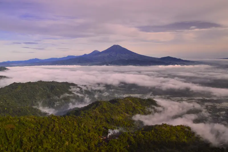 Lautan awan menutupi lembah Perbukitan Menoreh saat fajar dilihat dari Puncak Suroloyo, dengan siluet gunung di kejauhan