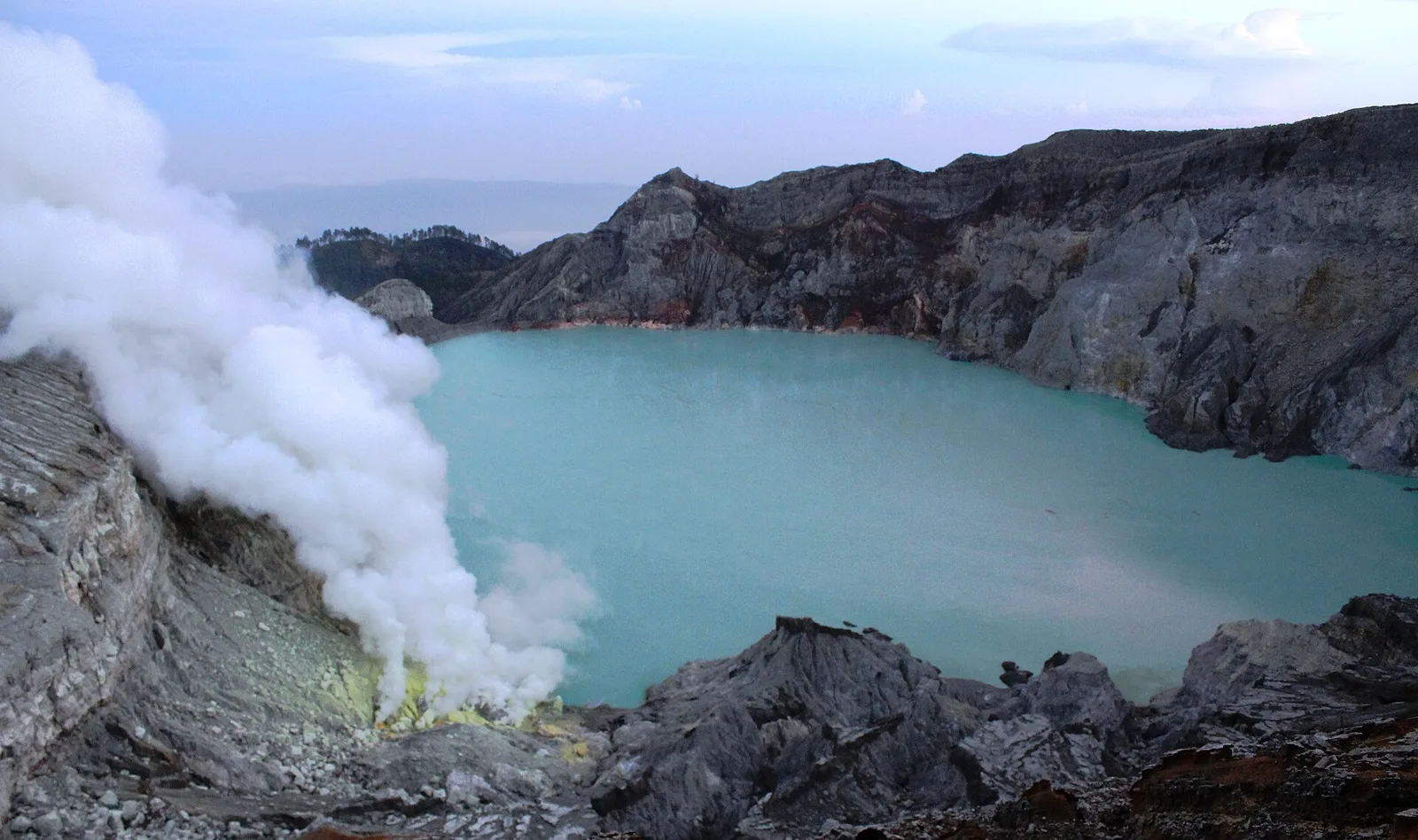 Danau kawah Ijen berwarna hijau toska dengan kepulan asap belerang tebal keluar dari sisi kawah berbatu di Banyuwangi