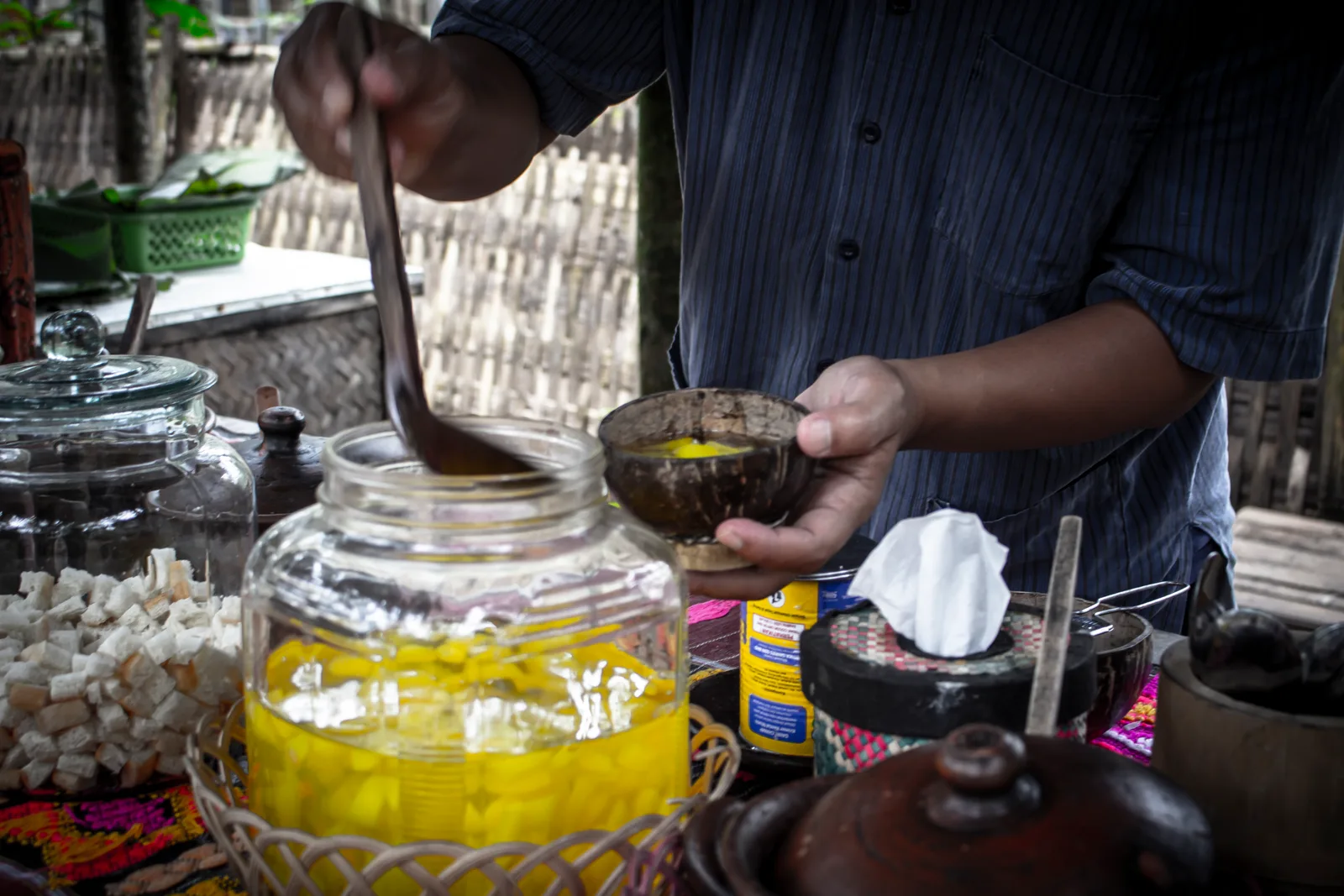 Penjual menyendok potongan buah carica kuning dari toples kaca ke dalam mangkuk batok kelapa di sebuah warung