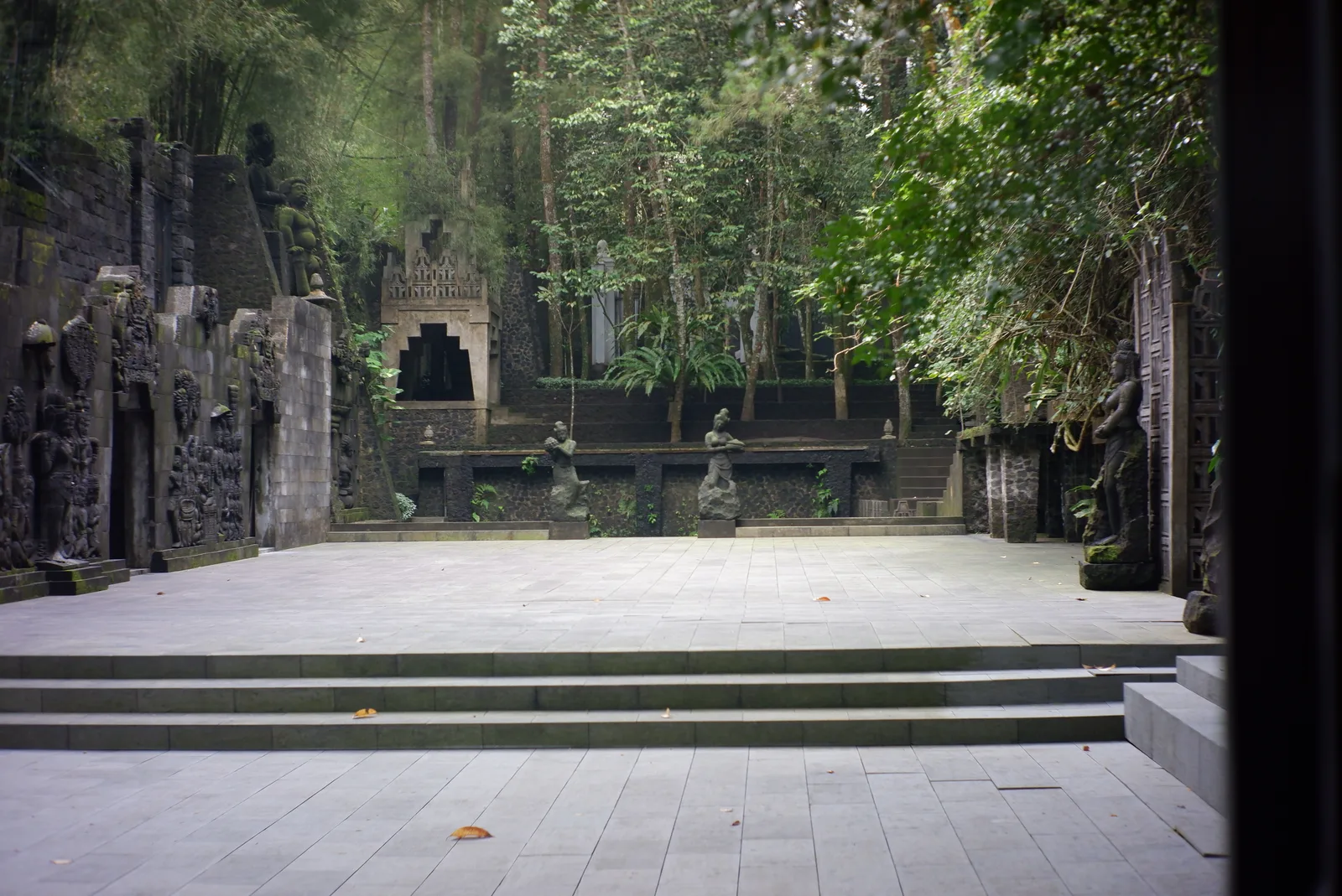 Pelataran batu Museum Ullen Sentalu di Kaliurang dengan dinding relief dan arca batu di antara pepohonan tinggi