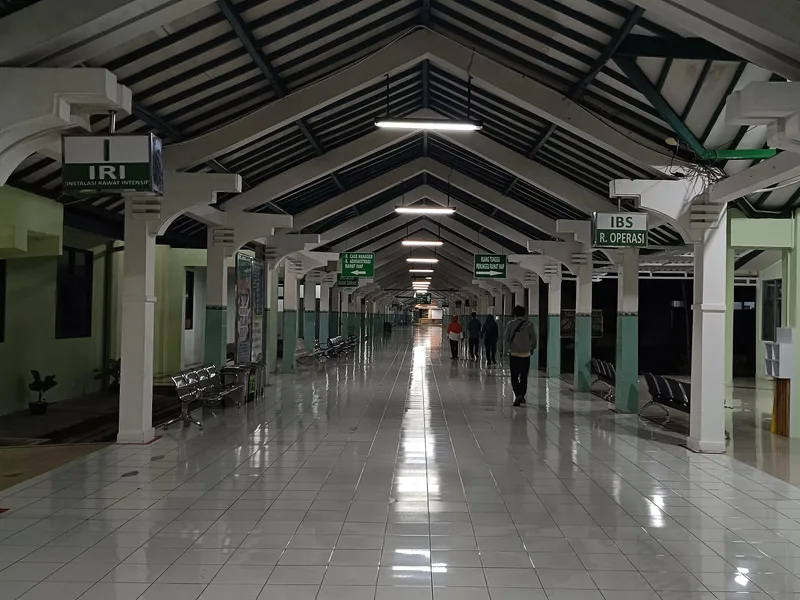 Lorong beratap panjang di rumah sakit daerah dengan papan penunjuk ruang rawat intensif dan instalasi bedah