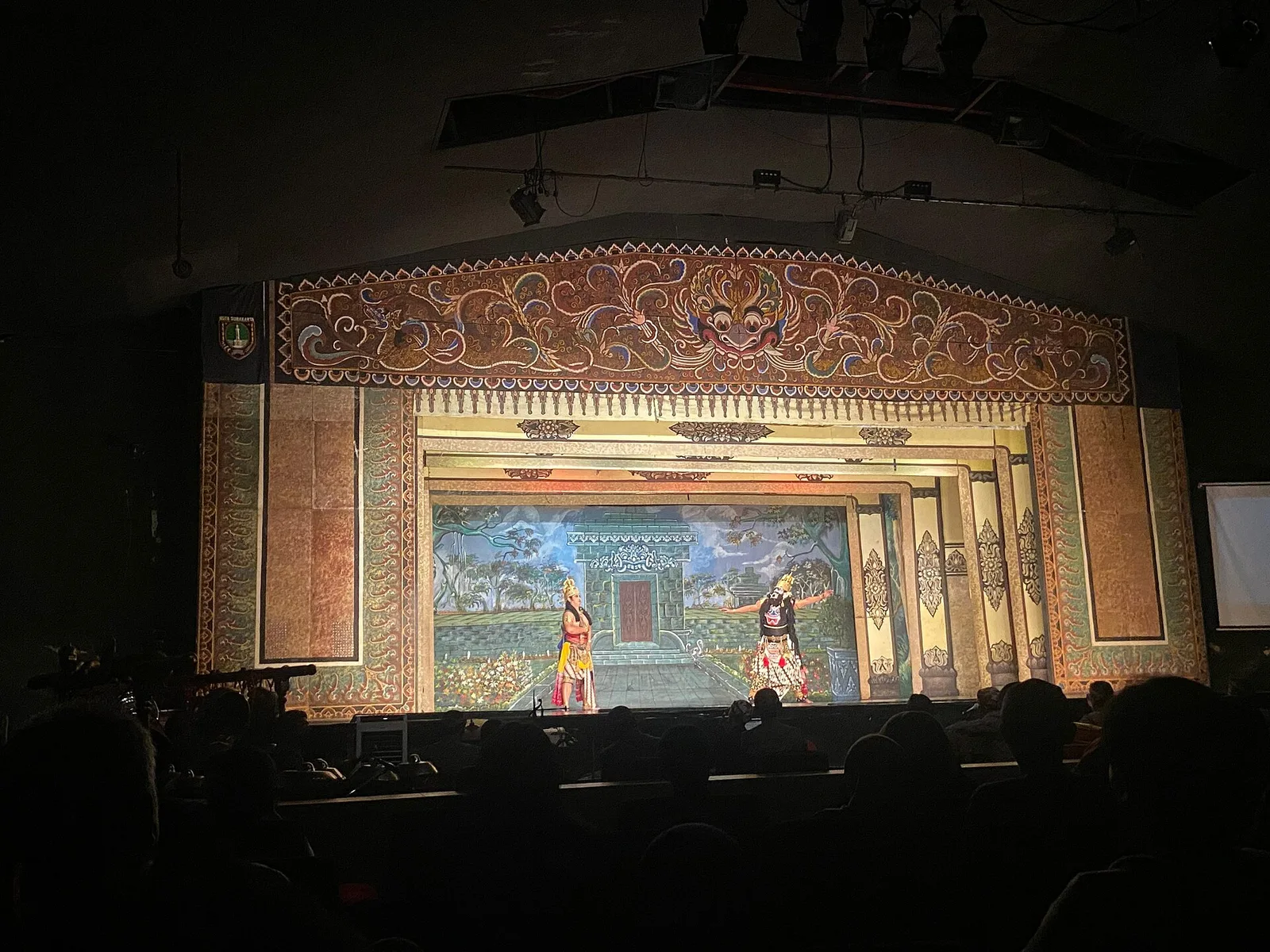 Pementasan wayang orang di panggung berhias ornamen Jawa di Gedung Wayang Orang Sriwedari Solo, dua penari di atas panggung dan penonton duduk dalam gelap